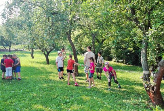 Deti plnia úlohu s lanom v záhrade medzi stromami Deti plnia úlohu s lanom v záhrade medzi stromami