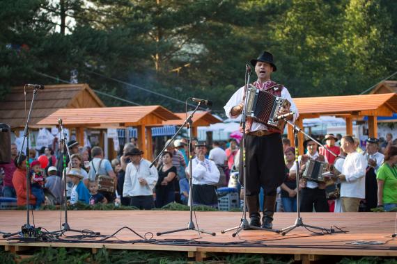 Na pódiu na jarmočnej scéne muzikant hrá na heligónke v pozadí ľudia Na pódiu na jarmočnej scéne muzikant hrá na heligónke v pozadí ľudia
