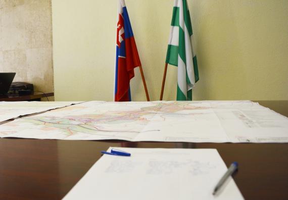 Na stole je papierový podklad územného plánu, v pozadí vlajky Slovenska a Detvy Na stole je papierový podklad územného plánu, v pozadí vlajky Slovenska a Detvy